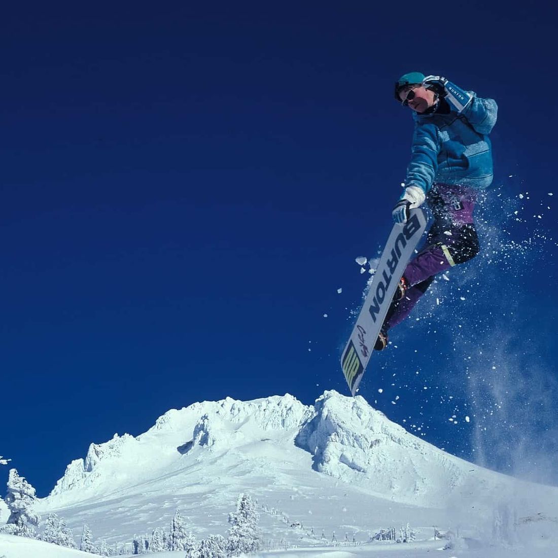 Person med blå vinterklær hopper med snowboard i vinterlandskap