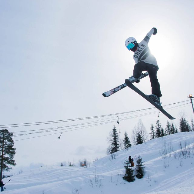 Person med hjelm og hvite klær hoper med ski i alpinanlegg